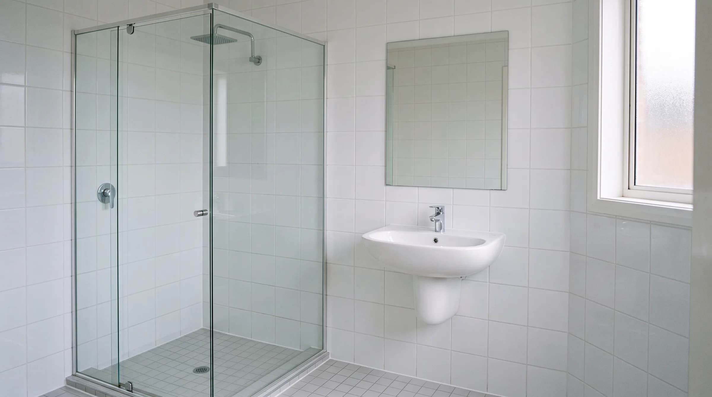 Frisch gereinigtes, leeres Badezimmer mit weissen Fliesen, Duschkabine und poliertem Waschbecken.